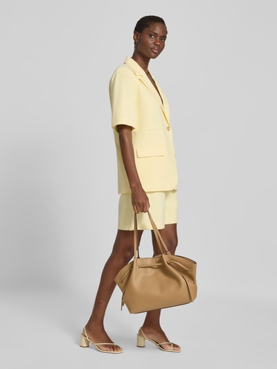 Frauenmodel trägt Handtasche mit Schulterriemen Modell 'Romina' von MANGO in Beige, strukturierte Oberfläche, Magnetverschluss, Ganzkörperansicht von vorne.