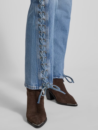 Frauenmodel trägt Straight Fit Jeans aus Baumwolle von ROTATE mit 5-Pocket-Design, hellblau, seitliche Zier-Einsätze in Zopf-Optik, Nahaufnahme Unterkörper.