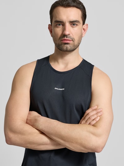 Männermodel trägt schwarzes, körpernahes Tanktop mit Rundhalsausschnitt Modell 'SHKOUT CORE' von Salomon, Mesh-Textur, Nahaufnahme Oberkörper.