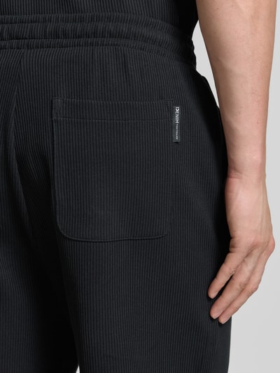 Mężczyzna nosi Relaxed Fit Sweatshorts aus reiner Baumwolle von Tom Tailor Denim, czarny rippstrick, tylna kieszeń, detal zbliżenie.