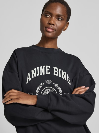 Frauenmodel trägt Oversized Fit Sweatshirt mit Logo-Print von Anine Bing aus reiner Baumwolle in Schwarz mit Rundhalsausschnitt, elastische Abschlüsse, Rückenlänge bei Größe S 61 cm, Nahaufnahme Oberkörper.