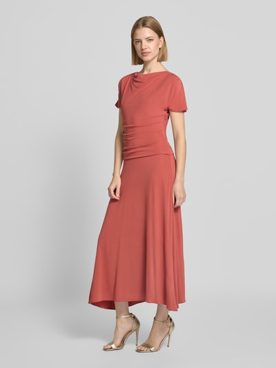 Frauenmodel trägt Cocktailkleid mit Wasserfall-Ausschnitt und Drapierungen von Christian Berg Cocktail in rostrot, A-Linie, Viskose-Elasthan-Mix, Midikleid, seitlicher Reißverschluss, fließende Textur, Ganzkörperansicht von vorne.
