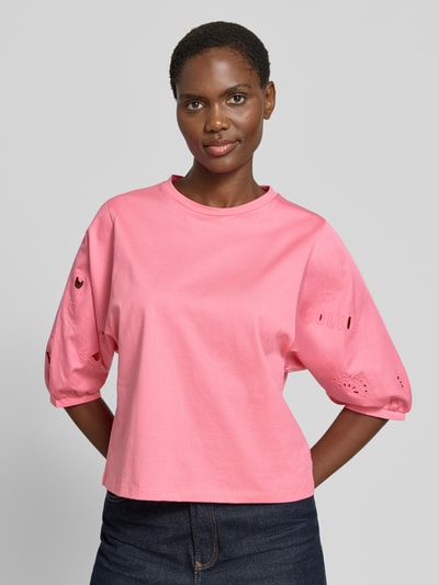 Kobiece model nosi T-Shirt mit 3/4-Arm und Lochstickerei von Marc Cain z bawełny, krój regular fit, rękaw o dł. 3/4, okrągły dekolt, długość tyłu w rozmiarze 36: 52 cm, różowy kolor, haft angielski, gładka faktura, całkowite ujęcie przodu.