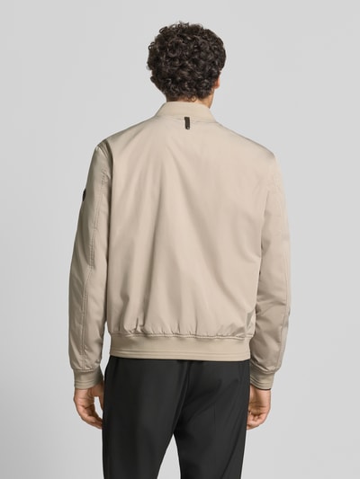 Męski model nosi Jacke mit Stehkragen und Reißverschluss Modell 'Arik' od JOOP! COLLECTION w kolorze beżowym, krój regular fit, stójka, wpuszczane kieszenie z zapięciem na zatrzask, Długość tyłu w rozmiarze 50: 66 cm, szerokość ramion w rozmiarze 50: 44 cm, szerokość klatki piersiowej w rozmiarze 50: 57 cm, długość rękawów w rozmiarze 50: 68 cm, widok całej sylwetki z tyłu