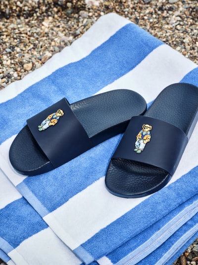 Produktfoto, Badeschuhe mit Polo-Bear-Print von Polo Ralph Lauren in Dunkelblau mit flacher Absatzform, abgerundete Schuhspitze, Applikation.