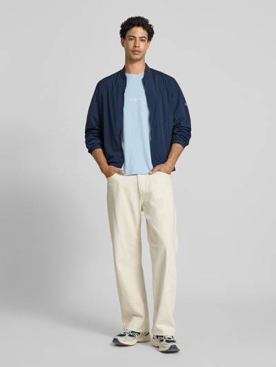 Männermodel trägt Regular Fit Bomberjacke mit College-Kragen Modell 'BELVEDERE' von Pepe Jeans, Optik: Unifarben, Label-Patch, Reißverschluss, seitliche Eingrifftaschen, Langarm mit elastischem Ärmelabschluss, cremige helle Hose und hellblaues Shirt, Farben: Dunkelblau, Weiß, Hellblau, Textur: glatter Stoff, Ganzkörperansicht von vorne.