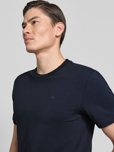 Męski model nosi T-Shirt z okrągłym dekoltem model 'Carlonito' od JOOP! Collection, bawełniany mix ze stretchem, krój straight fit, detal z logo, kolor ciemnogranatowy, zdjęcie zbliżenie na górną część ciała z przodu.