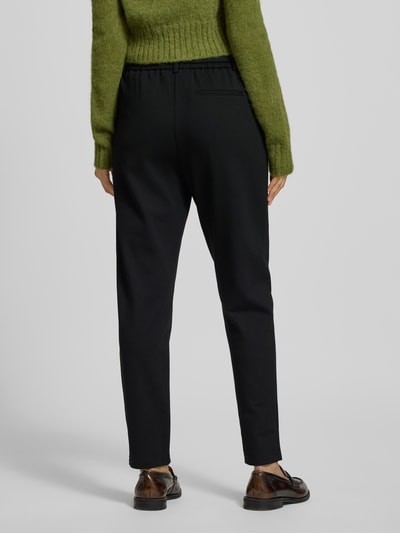 Vrouwenmodel draagt stoffen broek in viscosemix met stretch, los model, verkorte pasvorm, model 'Popye' van MSCH Copenhagen, binnenbeenlengte 75 cm, elastische band, stoffen riem, steekzakken, achterzak, zwart, textuur glad. Volledige lichaamsopname achteraan.