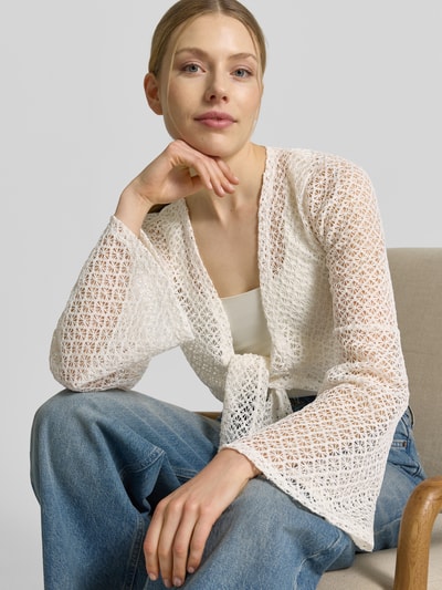 Frauenmodel trägt Strickjacke mit Knotendetail und Trompetenärmeln von Apricot, semitransparent, Cropped, Rückenlänge 43 cm, Nahaufnahme Oberkörper.