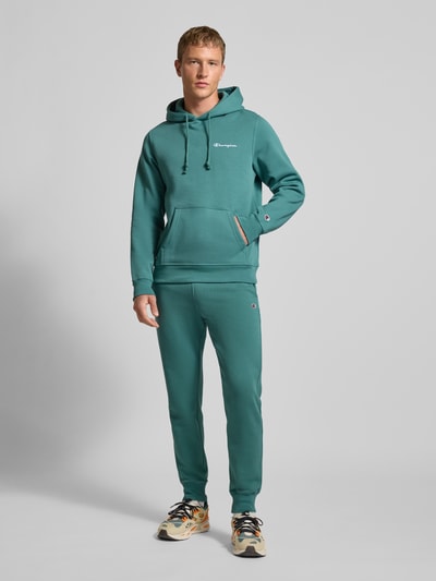 Männermodel trägt Hoodie mit Kapuze von CHAMPION in Türkis, Baumwoll-Mix, Lockerer-Schnitt, Känguru-Tasche, Label-Stitching, Gerippte-Abschlüsse, Ganzkörperansicht von vorne.