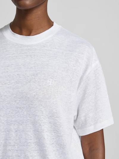 Vrouwenmodel draagt Regular Fit T-shirt uit zuiver linnen van Anine Bing, ronde hals, gestikt logo, korte mouw, maat S ruglengte 63 cm, close-up bovenlichaam.