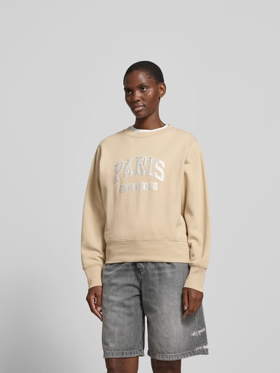 Frauenmodel trägt Sweatshirt aus reiner Baumwolle von Anine Bing in Beige mit Label-Detail, lockerer Passform, Rundhalsausschnitt, elastische Abschlüsse, Rückenlänge bei Größe S: 56 cm, Ganzkörperansicht von vorne.