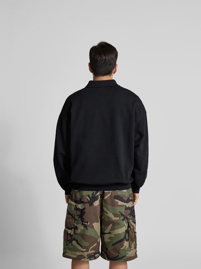 Männermodel trägt Regular Fit Poloshirt aus Baumwoll-Mix von VETEMENTS in Schwarz, kombiniert mit Camouflage-Shorts, Ganzkörperansicht Rückansicht. Herren Poloshirt aus Baumwoll-Elasthan-Mix, Relaxed Fit, Sweat, Polokragen, Rückenlänge bei Größe M: 71 cm.