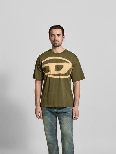 Männermodel trägt Regular Fit T-Shirt mit Logo-Print von Diesel in Olivgrün aus reiner Baumwolle, Rundhalsausschnitt, Kurzärmeliges Design, Rückenlänge bei Größe M: 68 cm, Ganzkörperansicht von vorne.