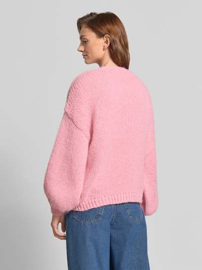 Frauenmodel trägt eine rosafarbene Loose Fit Strickjacke mit Ballonärmeln Modell 'MAYBE' von VERO MODA, grobe Stricktextur, Ganzkörperansicht Rückansicht.