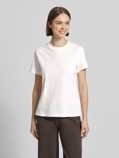 Frauenmodel trägt T-Shirt mit Label-Stitching und Rundhalsausschnitt von New Balance in Hellrosa, Reine Baumwolle, Regular-Fit, Rückenlänge 56 cm, Ganzkörperansicht von vorne.