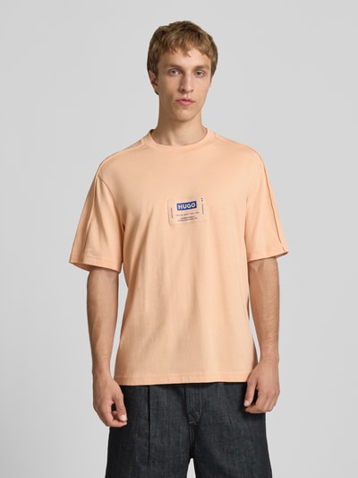 Männermodel trägt Regular Fit T-Shirt aus reiner Baumwolle Modell 'NURAZTI' von Hugo Blue in Unifarbe mit Label Patch, Ganzkörperansicht von vorne.
