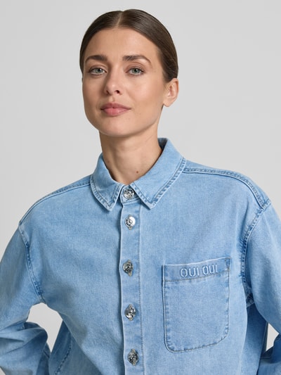 Vrouwenmodel draagt Relaxed Fit Jeansbluse mit Brusttasche van Oui, lichtblauwe denim, katoenmengsel met stretch, borstzak, hemdkraag, detailopname bovenlichaam.