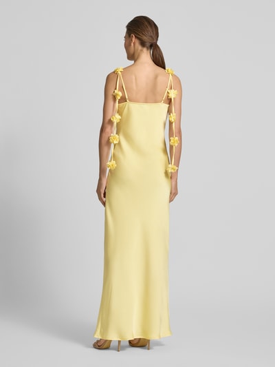 Frauenmodel trägt Fließendes Maxikleid mit Blumenapplikationen Modell 'ANALEI' von Vero Moda, Optik: Unifarben, Passform: fließend, Maxi, Wasserfall-Ausschnitt, Applikation: Blumen-Applikation, Trägerform: verstellbare Spaghettiträger, Materialverarbeitung: Satin, sanfte gelbe Farbgebung, glatte Satin-Textur, Ganzkörperansicht Rückansicht.