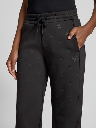 Frauenmodel trägt schwarze Wide-Fit Sweatpants mit Allover-Logo-Print Modell 'Calista' von Guess Activewear, Elastischer-Material-Mix, Elastischer Bund mit Tunnelzug, Detailaufnahme Nahaufnahme Oberkörper.