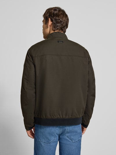 Männermodel trägt Blouson mit Stehkragen und Eingrifftaschen von camel active in dunklem Olivgrün, glatte Struktur, Ganzkörperansicht Rückansicht. Regular Fit, Reißverschluss und Label-Detail sichtbar.