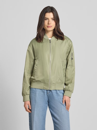 Kobiece model nosi Regular Fit Bomberjacke mit College-Kragen od s.Oliver RED LABEL, efekt: jednolity kolor, satyna, krój regular fit, kołnierz college, zamek błyskawiczny, zawieszka z logo, długi rękaw z prążkowanym zakończeniem, wpuszczane kieszenie i brustasza, wykończenie prążkowane, wykończenie materiału: satyna, kolor jasna oliwka, widok całej sylwetki z przodu.