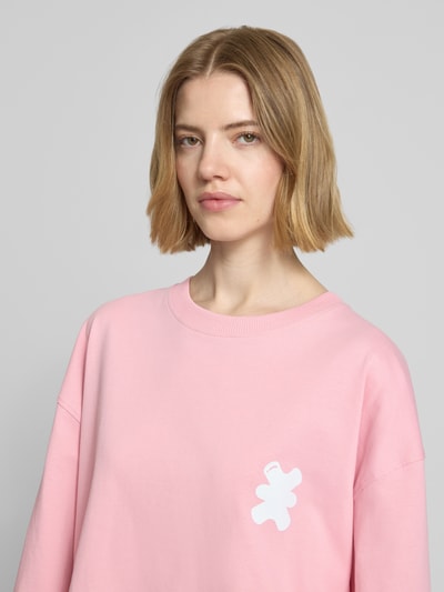 Frauenmodel trägt Sweatshirt mit Logo-Print von Karo Kauer in Rosa, reine Baumwolle, lockerer Schnitt, Rundhals, Nahaufnahme Oberkörper.