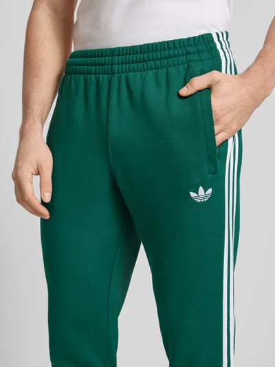 Männermodel trägt Sweatpants mit elastischem Bund von adidas Originals in Dunkelgrün mit weißen Streifen, Baumwoll-Elasthan-Mix, Nahaufnahme Oberkörper.