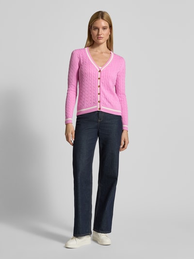 Modelka nosi Strickjacke mit V-Ausschnitt von Christian Berg Woman, bawełniany miks, krój regular fit, prążkowane wykończenia, różowy kolor, zapięcie na guziki, długość tyłu 58 cm, długość rękawa 66 cm; widok całej sylwetki z przodu.