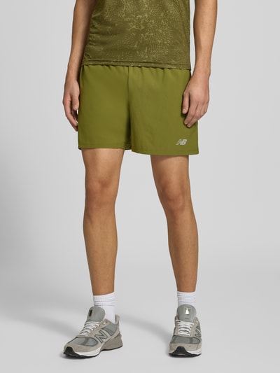 Männermodel trägt Shorts mit elastischem Bund und Logo von New Balance in Olivgrün, Regular Fit, Ganzkörperansicht von vorne.