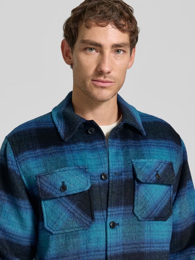 Männermodel trägt Regular Fit Hemdjacke mit Brusttaschen von Scotch & Soda, blau-schwarzes Karo mit Woll-Anteil, Nahaufnahme Oberkörper.