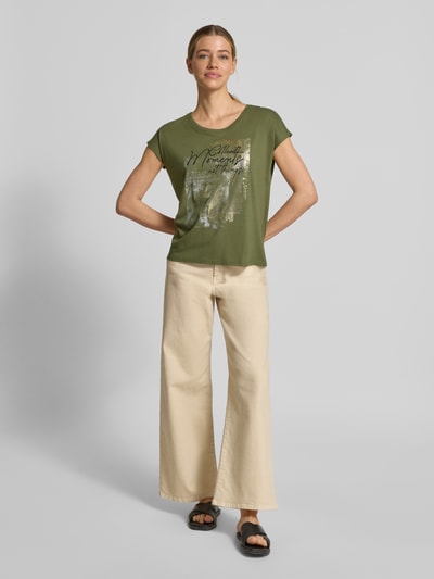 Frauenmodel trägt T-Shirt mit Motiv und Rundhalsausschnitt von Christian Berg Woman, olivgrün, Baumwoll-Viskose-Mix, Regular Fit, Ganzkörperansicht von vorne.