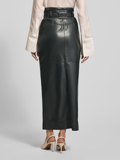 Frauenmodel trägt Eng anliegender Midi-Rock mit seitlichen Eingrifftaschen Modell 'VACARO' von BOSS Orange in Optik: Unifarben, Midi-Länge, Materialverarbeitung: Kunstleder, metallische Akzente, Label-Stitching-Applikation, Gehschlitz, Gürtelschlaufen, Bindegürtel; Ganzkörperansicht Rückansicht.