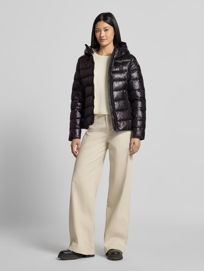 Frauenmodel trägt Jacke in Stepp-Optik Modell 'CAROLL' von Blauer USA in Schwarz mit Stehkragen und Kapuze, Ganzkörperansicht von vorne.