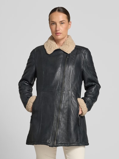 Modelka kobieca nosi Ledermantel mit Teddyfutter od Cabrini, naturalna skóra, prosty krój, podszewka ze sztucznego kożuszka, zamek błyskawiczny, kieszenie zapinane na zamek błyskawiczny, kolor czarny z beżową fakturą podszewki, widok całej sylwetki od przodu.