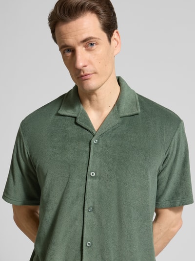 Męski model nosi Slim Fit Freizeithemd aus Frottee od MCNEAL, bawełniana mieszanka, krój slim fit, kołnierz rewersowy, frotte, krótki rękaw, długość tyłu w rozmiarze M: 71 cm, szerokość w rozmiarze M: 53 cm, długość rękawa w rozmiarze M: 24 cm, zielony, tekstura miękka, guziki na całej długości, zbliżenie na górną część ciała