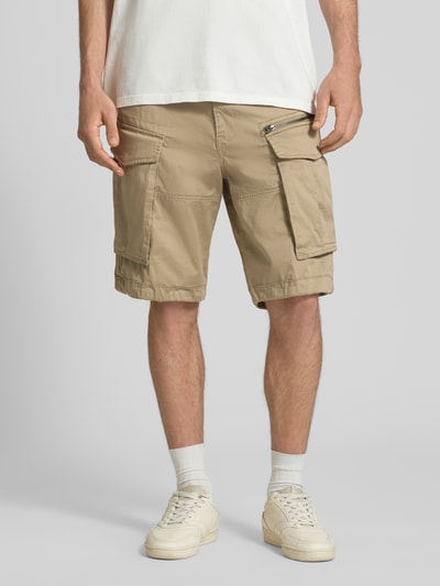 Männermodel trägt Bermudas mit Pattentaschen Modell 'ROVIC ZIP' von G-Star Raw, Baumwoll-Mix mit Stretch-Anteil, Straight Fit, 5-Pocket-Design, Knopf- und Reißverschluss, Patten- und Reißverschlusstaschen, Gesäßleistentaschen, beiger Farbton, strukturierte Oberfläche, Ganzkörperansicht von vorne.