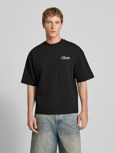 Männermodel trägt T-Shirt mit Logo- und Statement-Print von REVIEW, schwarze Reine Baumwolle, Loose-Fit, Rundhalsausschnitt, Ganzkörperansicht von vorne. Rückenlänge bei Größe M: 66 cm.