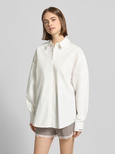 Frauenmodel trägt Oversized Hemdbluse mit Statement-Stitching Modell 'Leya' von OH APRIL aus Reine Baumwolle, Oversized-Fit, verdeckte Knopfleiste, Hemdblusenkragen, Ärmel mit Statement-Stitching, abgerundeter Saum, Rückenlänge bei Größe S 78 cm, Ärmellänge 61 cm, Weiß, glatte Struktur, Ganzkörperansicht von vorne.
