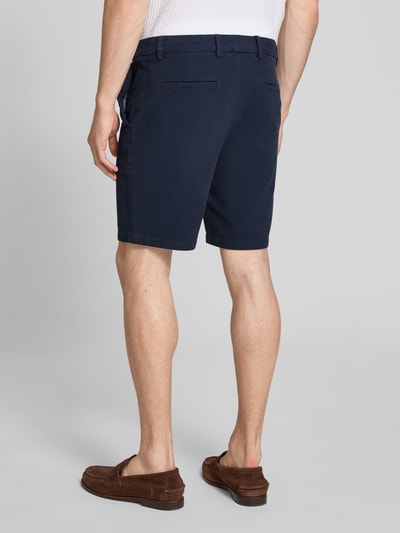 Männermodel trägt Modern Fit Chinoshorts aus Baumwoll-Mix Modell 'KANE1' von BOSS in Dunkelblau, unifarben, Ganzkörperansicht Rückansicht.