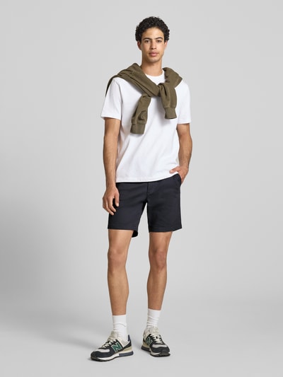 Männermodel trägt Straight Fit Shorts mit abnehmbarem Gürtel Modell 'Adam' von Jack & Jones aus Baumwoll-Mix, dunkle Farbe, Eingriff- und Gesäßtaschen, Knopf- und Reißverschluss, Ganzkörperansicht von vorne, Kontext: Herren Shorts, Bundweite 40 cm, Innenbeinlänge 19 cm bei Größe M.