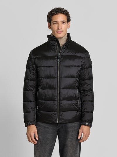Männermodel trägt Regular Fit Steppjacke mit Stehkragen von JOOP! COLLECTION in Schwarz mit glänzender Oberfläche, Ganzkörperansicht von vorne.