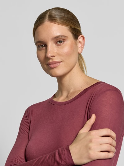 Vrouwenmodel draagt Longsleeve in semitransparente look van Anine Bing, lyocell- en lamswolmix, aansluitende fit, ronde hals, bordeauxrood, textuur licht doorschijnend, detailopname bovenlichaam.
