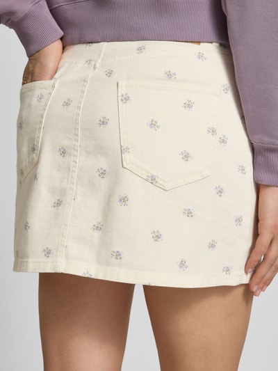 Frauenmodel trägt Ausgestellter Mini-Rock aus reiner Baumwolle Modell 'NAOMI' von Only mit Florales-Allover-Muster, Twill, Label-Patch, Knopfleiste, Gesäßtaschen und seitliche Eingrifftaschen, Creme mit kleinen Blumen, Nahaufnahme Rückansicht.