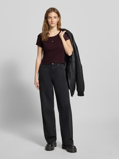 Modelka nosi Cropped T-Shirt mit Label-Detail od Calvin Klein Jeans, bawełna z elastanem, krótki fason, okrągły dekolt, tył 43 cm w rozmiarze S, całopostaciowy widok z przodu.