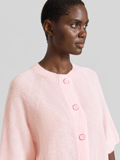 Männermodel trägt Regular Fit Cardigan aus Mohair-Alpaka-Mix in Strick-Optik von Marc Cain, różowy, półokrągły dekolt, półrękaw, guziki, Nahaufnahme Oberkörper. Regular Fit, długość tyłu 54 cm, długość rękawa 38 cm.