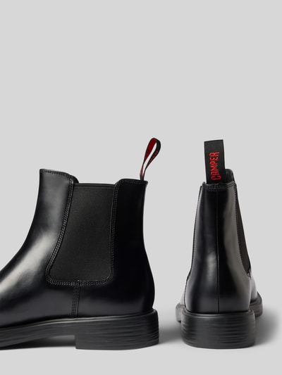 Produktfoto, schwarze glänzende Boots aus echtem Leder Modell 'Dean' von Camper, abgerundete Form, Logo-Detail, strukturierte Sohle