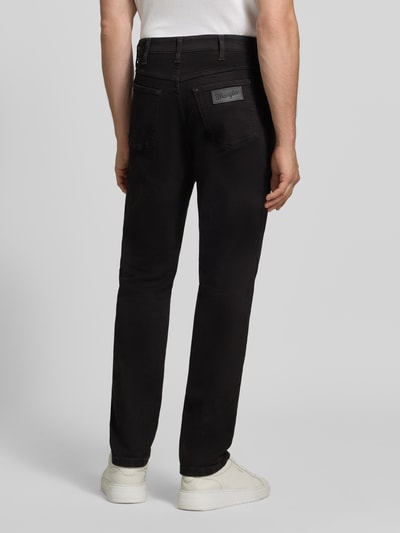 Männermodel trägt schwarze Tapered Fit Jeans aus Baumwoll-Mix Modell 'Redford' von Wrangler, Ganzkörperansicht Rückansicht, Herren Tapered Fit Jeans.