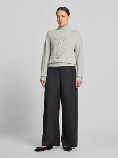 Vrouwenmodel draagt gebreide pullover met opstaande kraag van Christian Berg Woman, los model, ribboorden, oversneden schouders, met lange mouwen, ruglengte maat M: 58 cm, mouwlengte maat M: 60 cm, effen lichtgrijs, zachte textuur, effen zwarte wijde broek, voorkant volledig zichtbaar, Ganzkörperansicht von vorne.