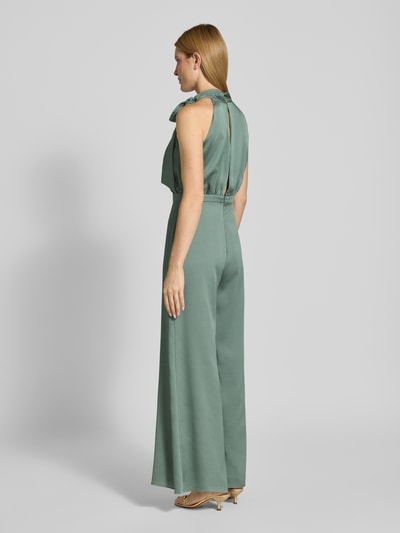 Frauenmodel trägt Jumpsuit mit Schleifen-Detail von SWING in Grün, Regular-Fit, Neckholder, Rückseitiger Reißverschluss, Ganzkörperansicht Rückansicht, Rückenlänge bei Größe 36: 40 cm, Brustweite: 36 cm, Gesamtlänge: 152 cm, Innenbeinlänge: 83 cm.